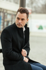 the man sits at a stop. On him a black classical coat. He looks in a distance and is shipped in the thoughts.