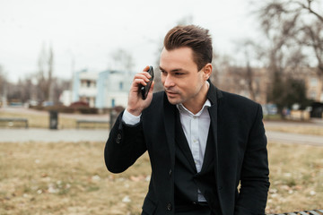 the man sits on a bench and resolves issues in phone. At phone of a problem with communication. He has on a face a faint smile and the interested look.