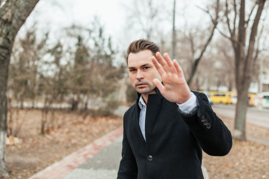 the man in a strict suit and a coat walks. He it is obvious against photos. He has quite severe look.