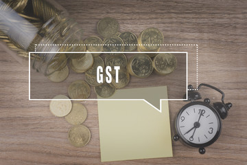 Coins spilling out of a glass jar on wooden background with GST as Goods and Services Tax text . Financial Concept