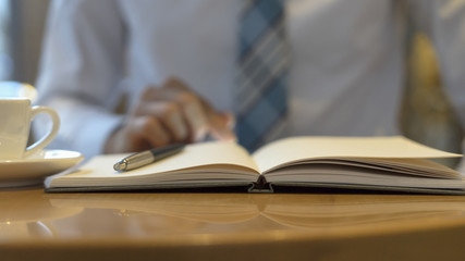 Male hand holding ready to make note, looking at cellphone. Businessman or employee at workplace writing business ideas, plans or tasks at personal organizer.