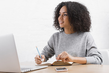 Young woman taking notes at a table with laptop and smartphone