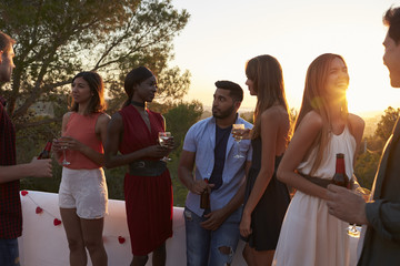 Young adult friends talk at a party on a rooftop at sunset