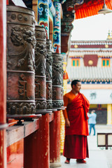 QINGHAI, CHINA - October 4, 2016: Tibetan monk standing near the prayer wheels in the ancient...