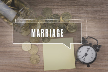 Coins spilling out of a glass jar on wooden background with MARRIAGE text . Financial Concept