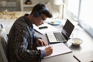 Fototapeta na wymiar Teenage boy wearing headphones works at desk in his bedroom