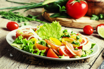 Salad with avocado, salmon, lettuce, onions and peppers on a pla