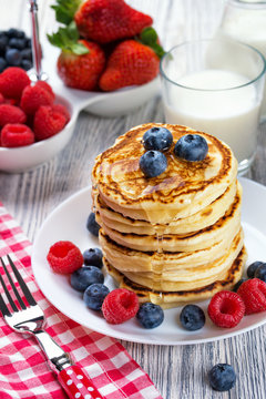Stack of pancakes with fresh blueberry and raspberry, poured with honey. Milk and fresh berries, healthy breakfast concept