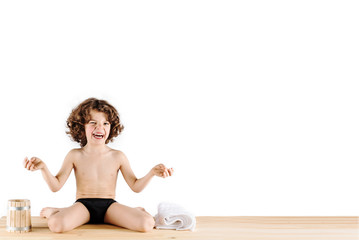 Cute curly-haired boy in shorts sitting in a "position of the Hero" and laughs. White background. © kravik93