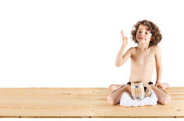 Cute curly-haired boy in shorts sitting in a "Hero of the position," raised his hand bent at the elbow. Before him is a wooden mug and towel. White background. © kravik93