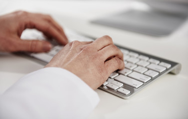 Woman practitioner typing medical report on keyboard at the desk. 
