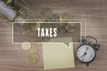 Coins spilling out of a glass jar on wooden background with TAXES text . Financial Concept