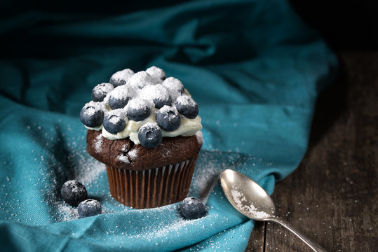 Chocolate muffin with soft cream and fresh blueberry powdered with sugar, rustic background