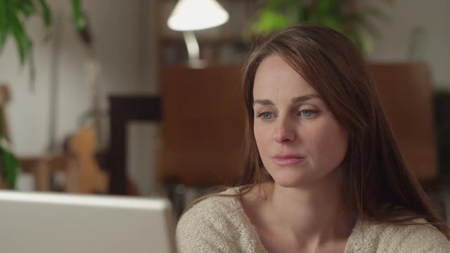 Young woman watches videos on internet in her laptop at home. She watches very concentrated and indignanted. She denies shaking her head. Dolly shot to the left.