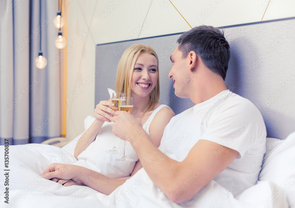 Poster smiling couple with champagne glasses in bed