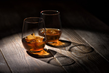 Two glasses of whisky with ice on the nature wooden table