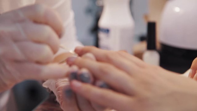 Hands in medical gloves doing manicure procedure on fingers with wedding ring in beauty shop