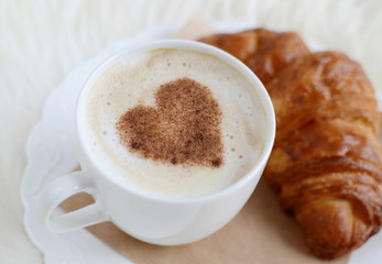 Cup of cappuccino with heart pattern of cinnamon with yummy croissant