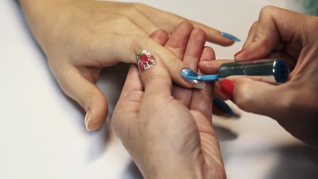 Beauty salon manicure session, female hand painting finger nails blue polish, close up