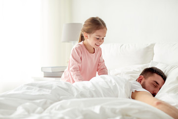 little girl waking her sleeping father up in bed