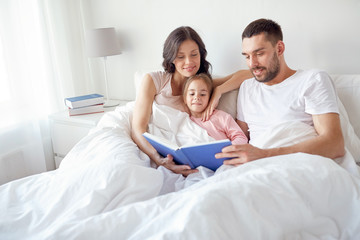 Obraz na płótnie Canvas happy family reading book in bed at home