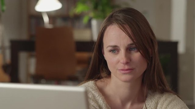 Young woman watches videos on internet in her laptop at home. She watches very concentrated and serious with a suddenly look of disgust. Dolly shot to the right.