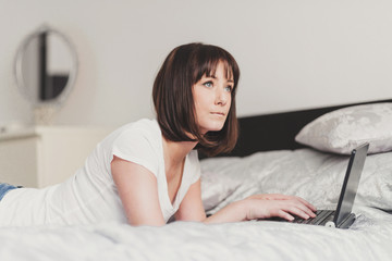 beautiful woman works on laptop in bedroom
