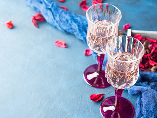 Two stemmed champagne glasses on blue textured background with pink dried flowers. Valentine's day wedding romantic date invitation