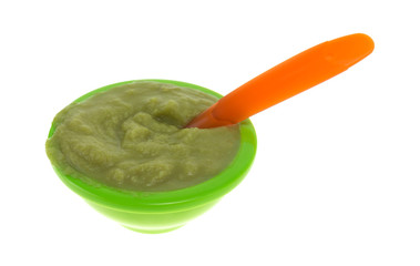 Green peas baby food mush in a bowl with a spoon isolated on a white background.