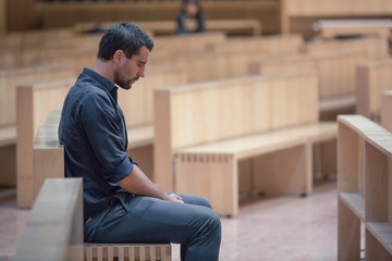 Young beard man wearing blue shirt praying in modern church