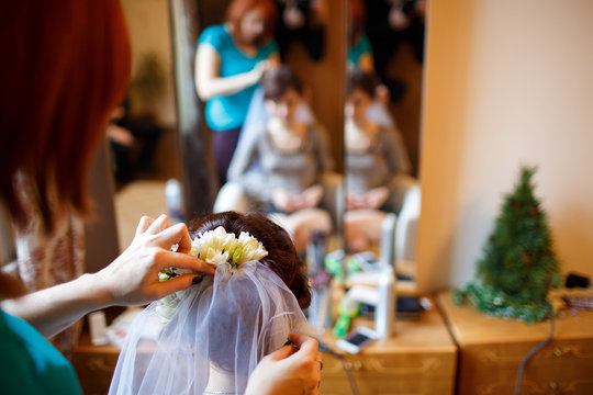 Young beautiful bride getting her hairstyle, braiding roses in h