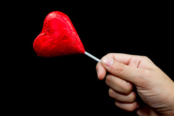 Hand holding red heart chocolate and black background. Valentine