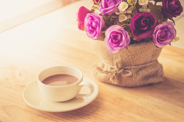 Happy weekend concept. White cup of coffee on wooden floor with purple flower in pot vintage color tone.