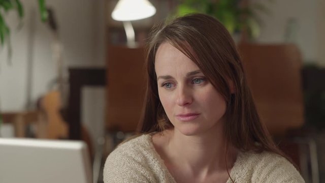 Young woman watches videos on internet in her laptop at home. She watches very concentrated and serious with a suddenly look of disgust. Dolly shot to the left.