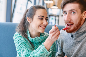 couple eating a dessert in a cafe on a date and drinking coffee. woman and man looks at a spoon with cake and smiling. Love story and Valentines.