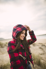 Smiling young woman with long brown hair wearing hooded jacket on the beach