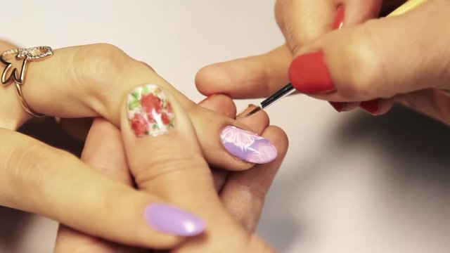 Beauty shop manicure session, woman hand painting floral pattern on nail varnish, close up