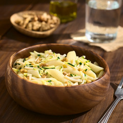 Penne pasta with zucchini and ham stripes and walnut served in wooden bowl, photographed on dark wood with natural light (Selective Focus, Focus in the middle of the dish)