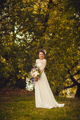 Obraz na płótnie Canvas Beautiful stylish bride in a beautiful dress with flowers in the park