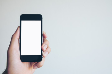 Mockup image of hand holding black mobile phone with blank white screen on white background room