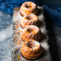 Mini bundt ring cakes with orange zest icing sugar on dark blue background and serving board. Holiday sweet food