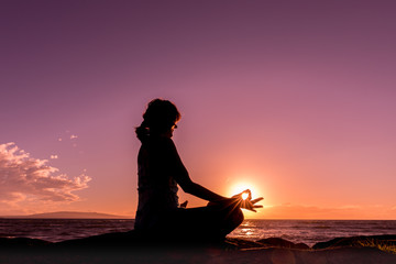 Fototapeta premium Woman Silhouetted Practicing Yoga on the Beach at Sunset