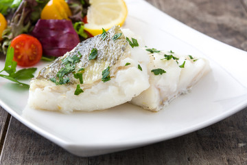 Fried cod fillet and salad in plate on wooden background
