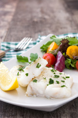 Fried cod fillet and salad in plate on wooden background
