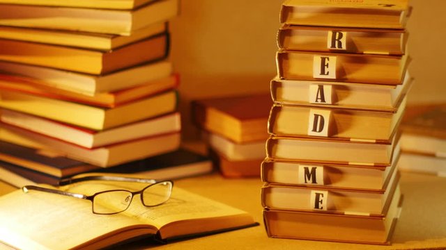 The phrase READ ME described with letters on stack of books. A pile of books with the words 'read me' appears on the table near the open book with glasses. Stop motion