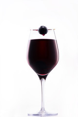 Wine dripping from red grape on top of classy glass of red wine;