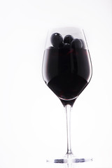 Glass of red wine filled with grapes in on white background