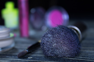 Makeup brush and cosmetics on wooden table and black background behind, beautiful bokeh.