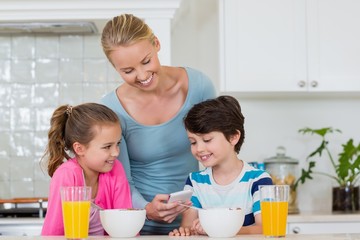 Mother showing mobile phone to kids while having breakfast