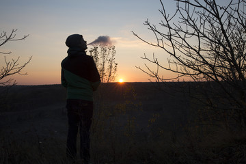 The young beautiful boy vaper against the sunset